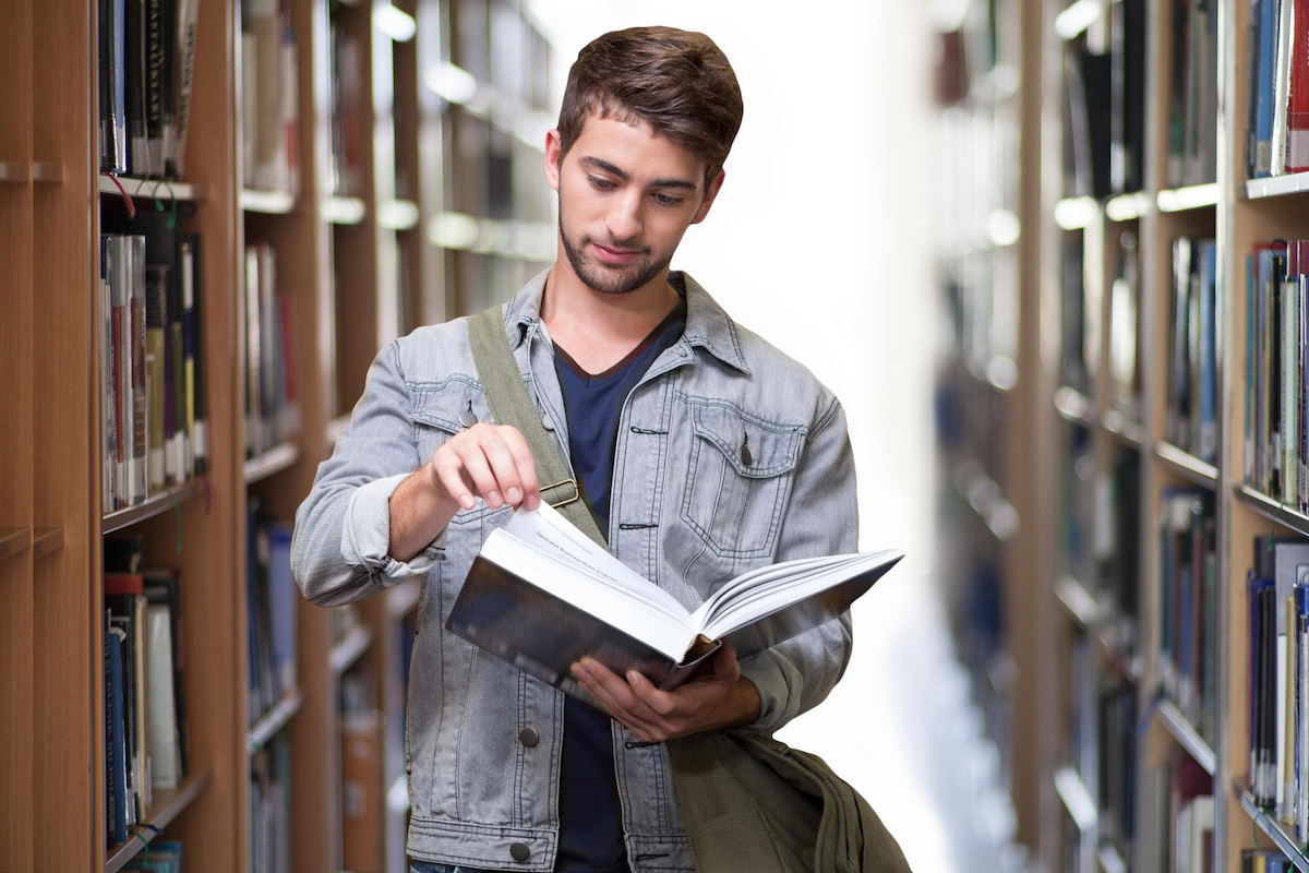 How to choose a uni degree. Young man in a university library flicking through a textbook.