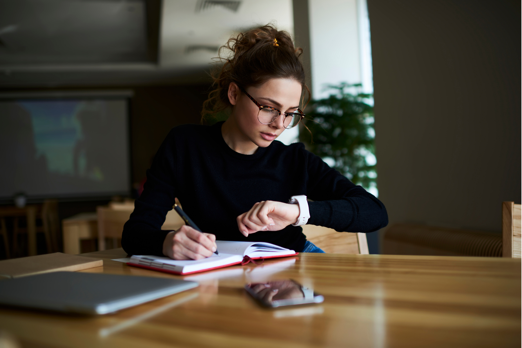student checks the time on her watch whilst studying at her desk
